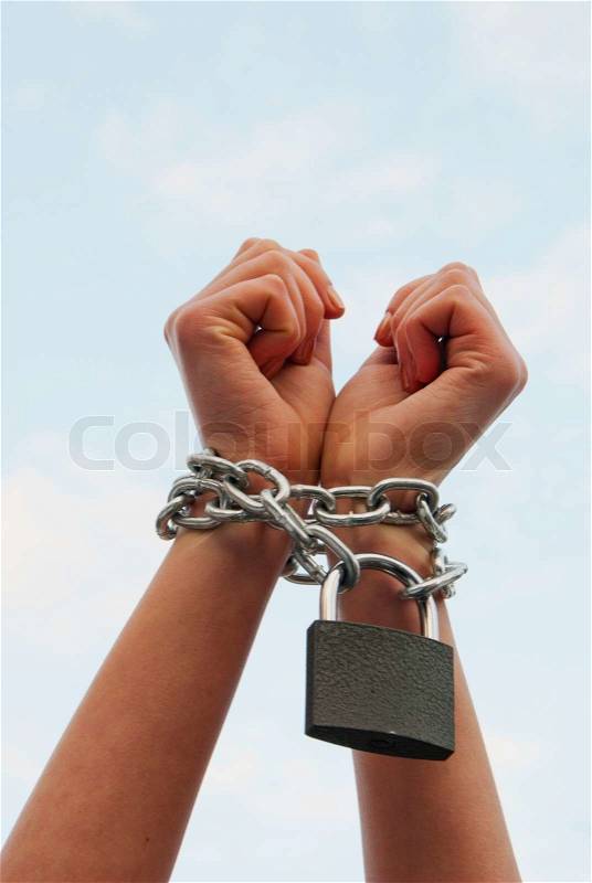 Woman\'s hands tied up with chains against blue sky, stock photo