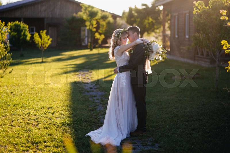 Side view of happy beautiful wedding couple hugging on green lawn, stock photo