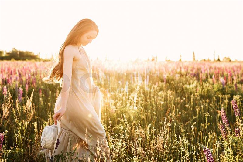 Young woman walking in lupine flower field with sunrise on the background. Warm orange sunbeam light, stock photo
