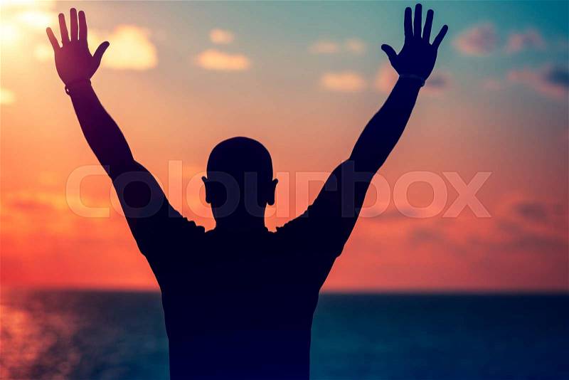 Silhouette of happy man with raised up hands standing on the beach on sunset, enjoying freedom and summer holidays , stock photo