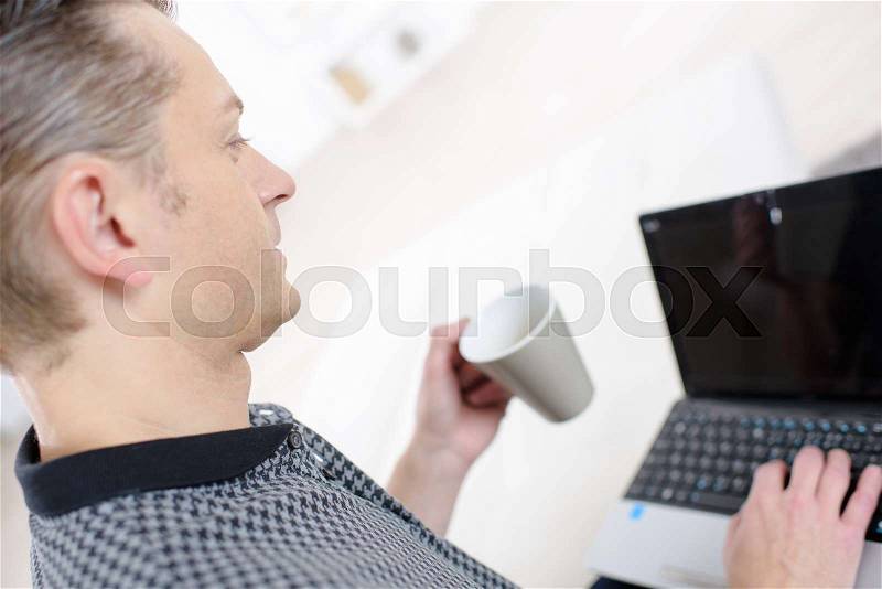 Happy man with laptop in kitchen, stock photo