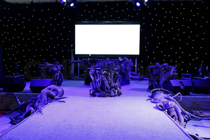 Big blank screen on purple show event stage decorated with tree roots, stock photo