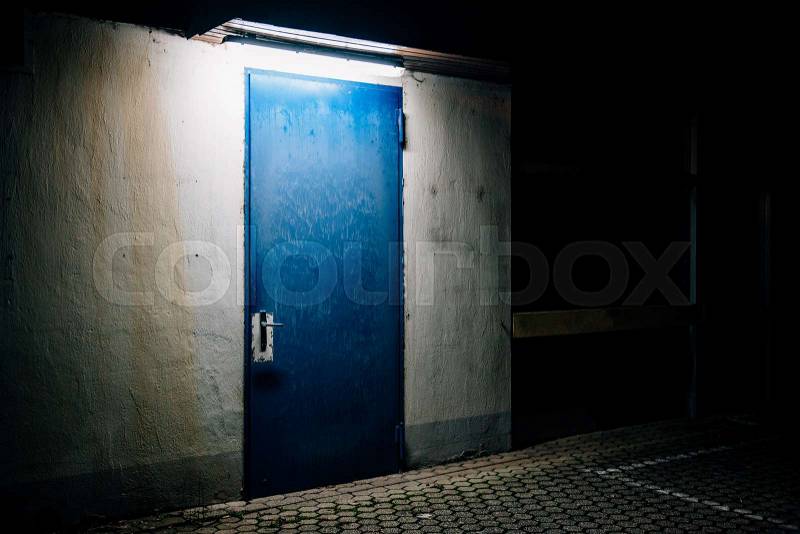 One blue door in the darkness illuminated from the above in empty city, stock photo