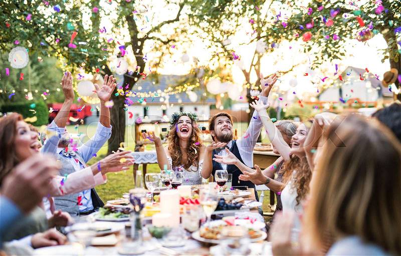 Wedding reception outside in the backyard. Bride and groom with family and guests sitting around the table, having fun, stock photo