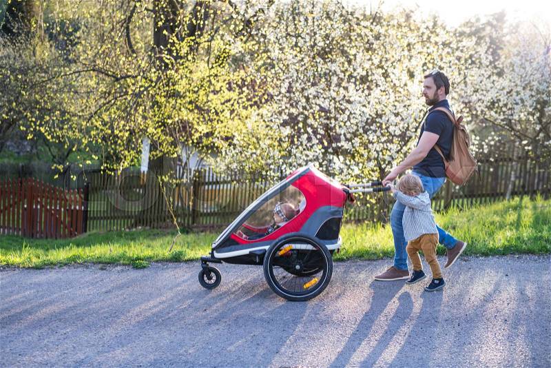 A father with toddler son pushing a jogging stroller outside. A walk in spring nature, stock photo