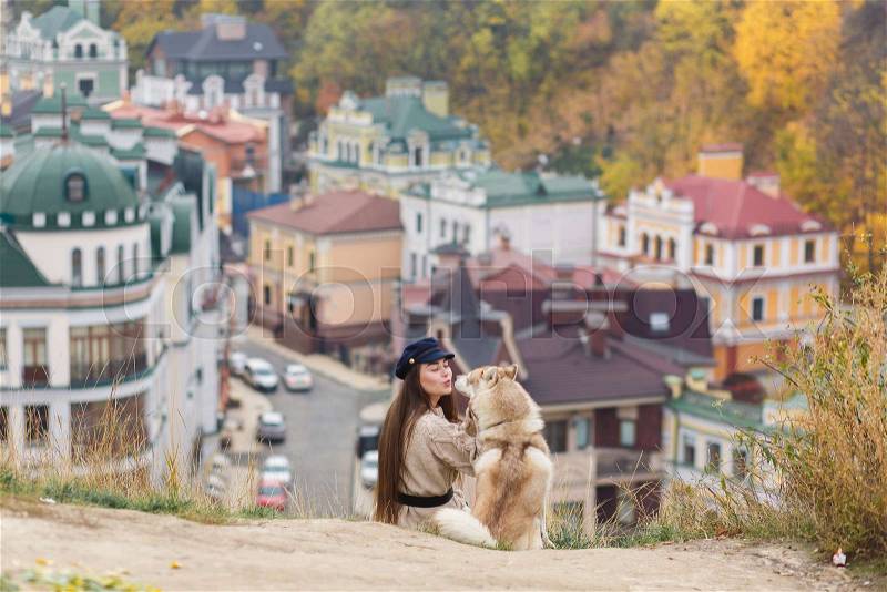 Young long hair woman hugging her dog husky in sunny summer beautiful day sitting on old town background, stock photo
