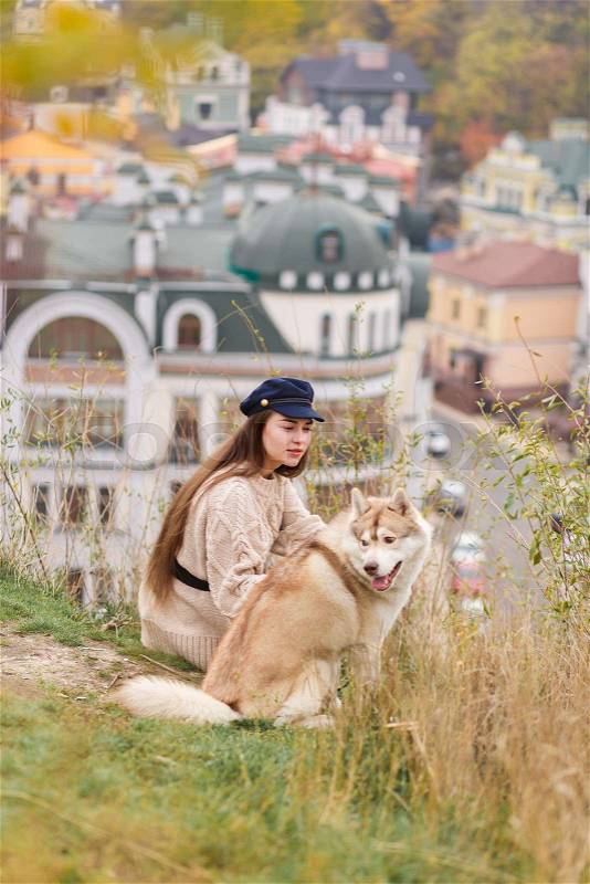 Back view of a young woman sitting with her dog on old city buildings streets background, stock photo