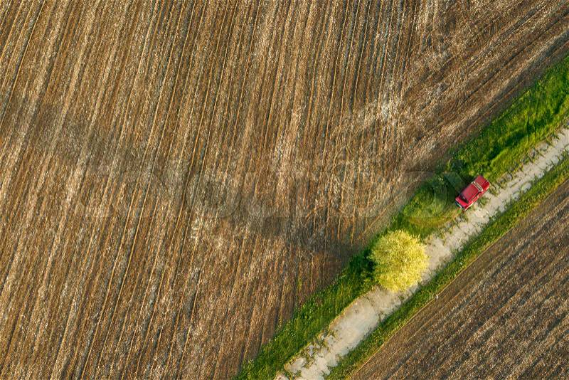 Abstract geometric forms of agricultural field soil without crop sowing, separated diagonally by road and red car on it, in green and black colors. A bird\'s eye view from the drone, stock photo