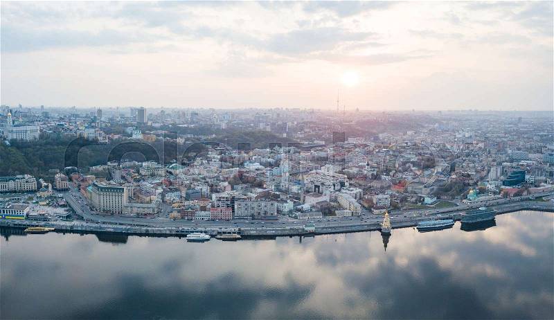 Aerial panoramic view from the drone on the central historical part of the city Kiev, and the district of Podol with the Postal square, hotels, churches, river Port. Reflection of sunset and cloudy sky in the Dnieper River, stock photo