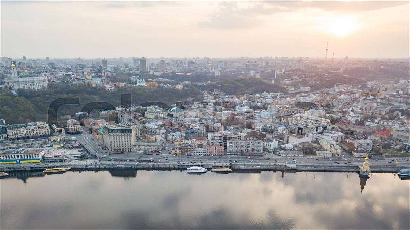 Aerial panoramic view from the drone on the central historical part of the city Kiyv, and the district of Podol with the Postal square, hotels, churches, river port. Reflection of sunset and cloudy sky in the Dnieper River, stock photo