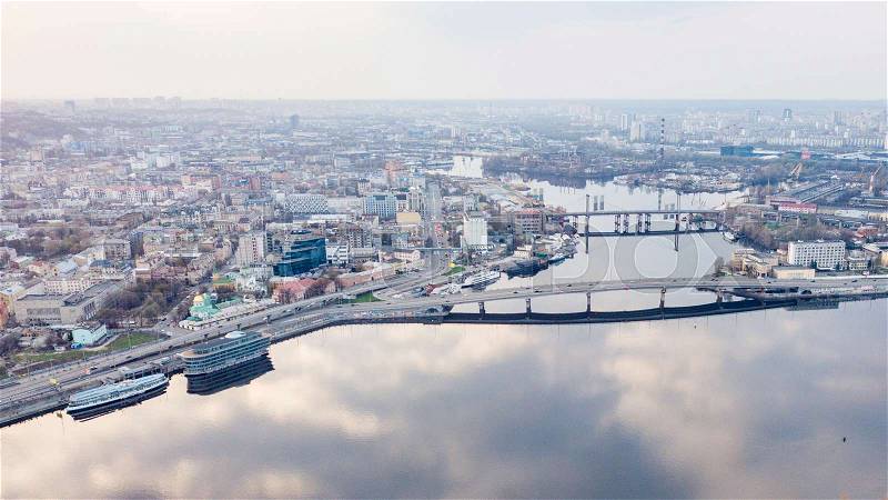 Aerial panoramic view from the drone on the central historical part of the city Kiyv and the district of Podol with Rybalskiy Island, churches, the ships, river docks and Havana bridge. Reflection of sunset and cloudy sky in the Dnieper River, stock photo
