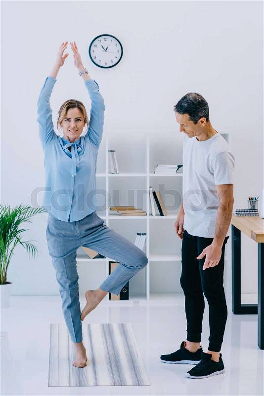 Businesswoman with her trainer practicing yoga in tree pose at office, stock photo