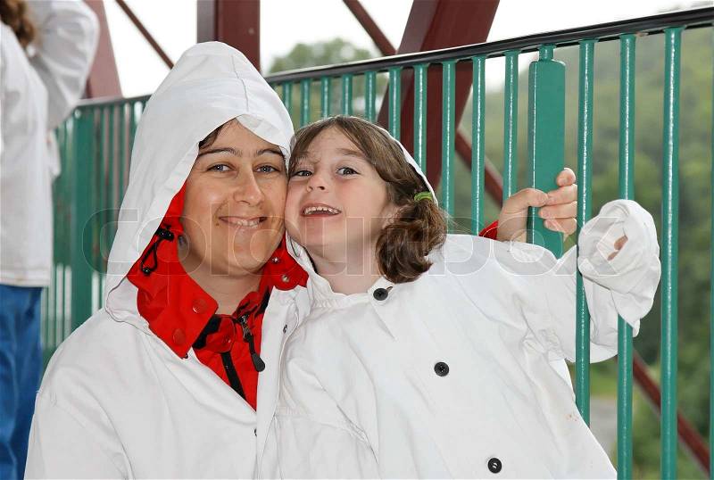 Loving mother and cute preschool daughter in white cloaks with hoods on a bridge, stock photo
