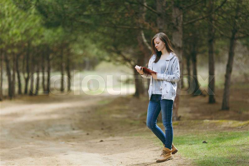 Young calm beautiful woman in casual clothes studying reading book standing in big city park or forest on green blurred background. Student learning, education. Lifestyle, leisure concept, stock photo