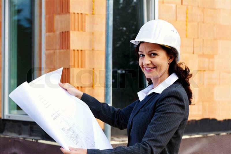 Architect with blueprint before shell of a house building a house, stock photo