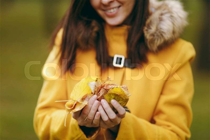 Beautiful happy caucasian young smiling brown-hair woman in yellow coat, jeans, boots in green forest. Close up model with fall golden leaves standing and walking in early autumn park outdoors, stock photo