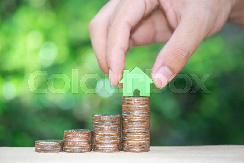 Man hand is put the home model to growing coin stack for concept of money saving for home buying fund, stock photo