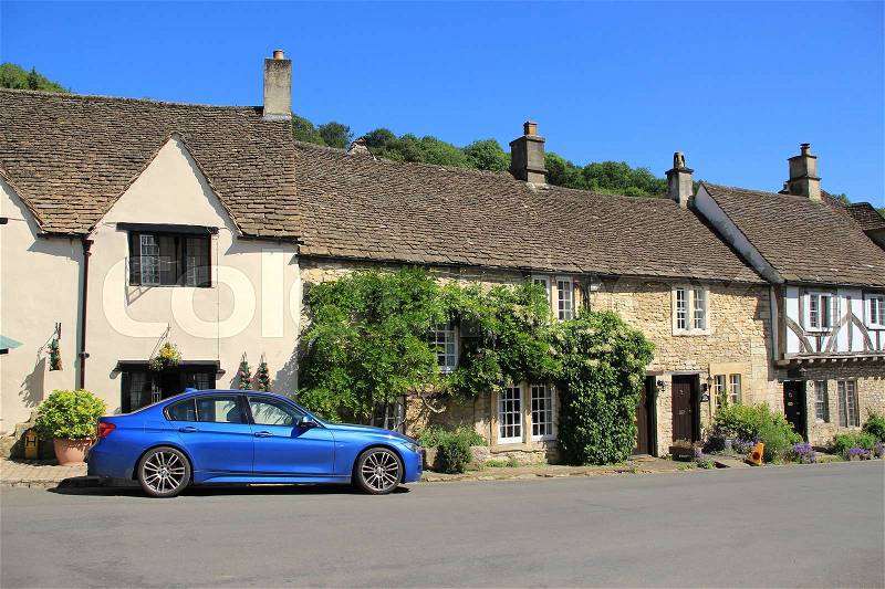 A striking blue car in one of the streets in the village Castle Combe in the Cotswolds in England on a sunny day in spring, stock photo
