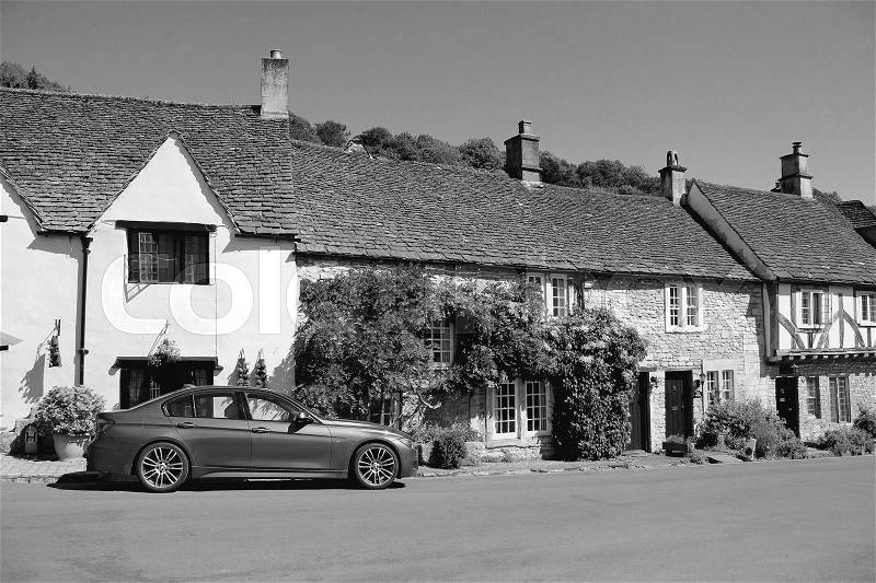 A car in one of the streets in the village Castle Combe in the Cotswolds in England on a sunny day in spring in black and white, stock photo