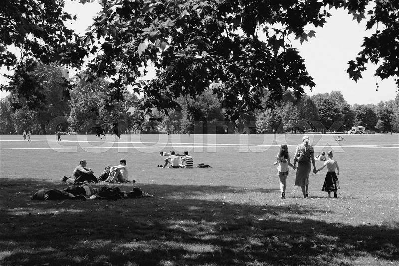 People are sitting and a mom is walking hand in hand with her daughters over the lawn in Hyde Park in the city London in England on a sunny day in spring in black and white, stock photo