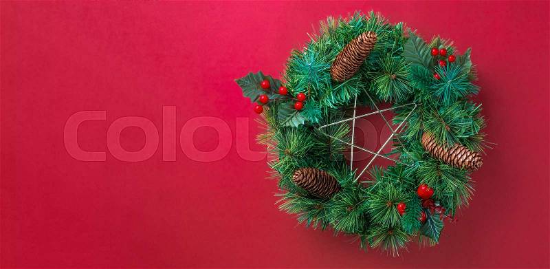 Green pine christmas wreath with star and pine cone ,cherry decoration item on red wall background.copy space for adding text or design.Celebration holiday festive greeing card, stock photo