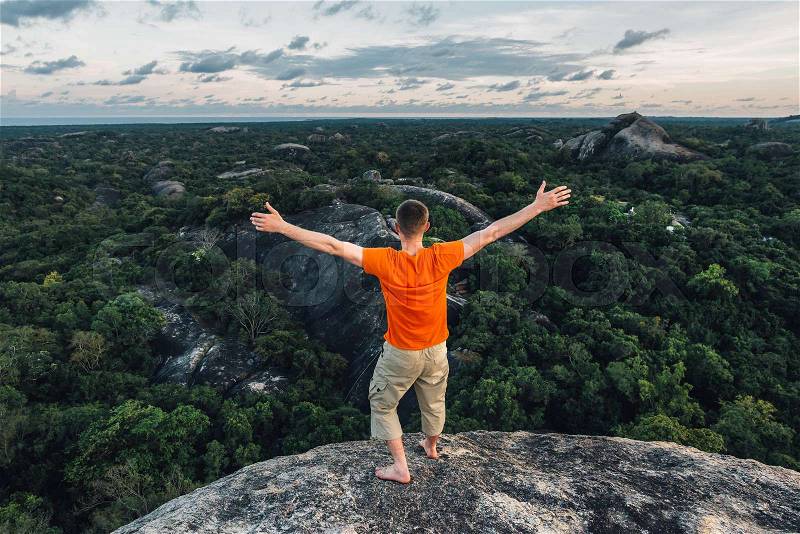 Happy man in orange T-shirt standing with open arms on the big stone in the forest, stock photo