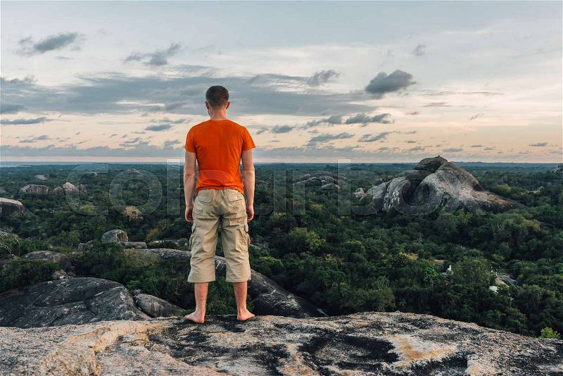 Happy man in orange T-shirt standing and look beautiful view on the big stone in the forest, stock photo