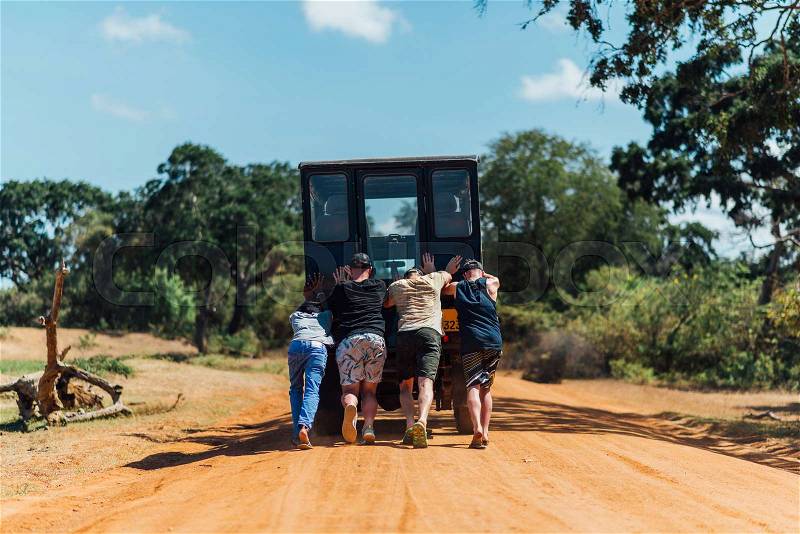 Four people pushing their car that stuck in the yellow sand in savannah, stock photo