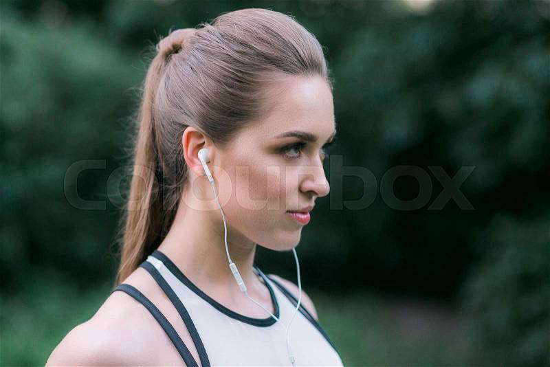 Female athlete wearing earphones. Woman listening to music during workout outdoor. Close up face shot, stock photo