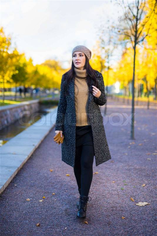 Young beautiful woman in warm clothes walking in autumn park, stock photo