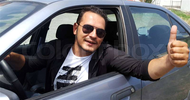 Young man doing thumps-up in car, stock photo