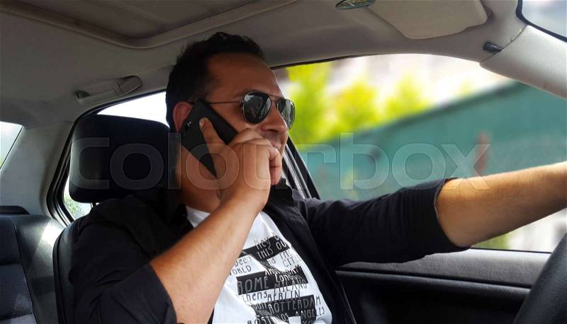 Young man talking on his phone and driving a car, stock photo