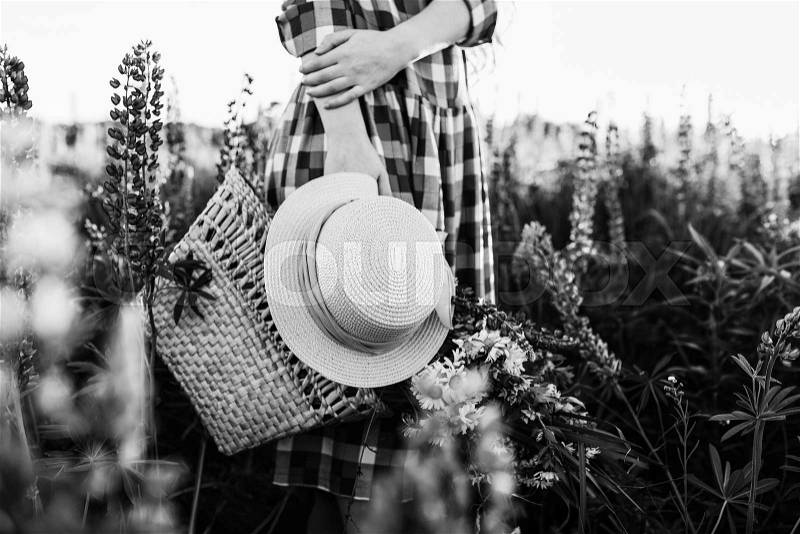 Woman holding straw bag and hat, standing in flower field at sunset. Close-up view noface, stock photo