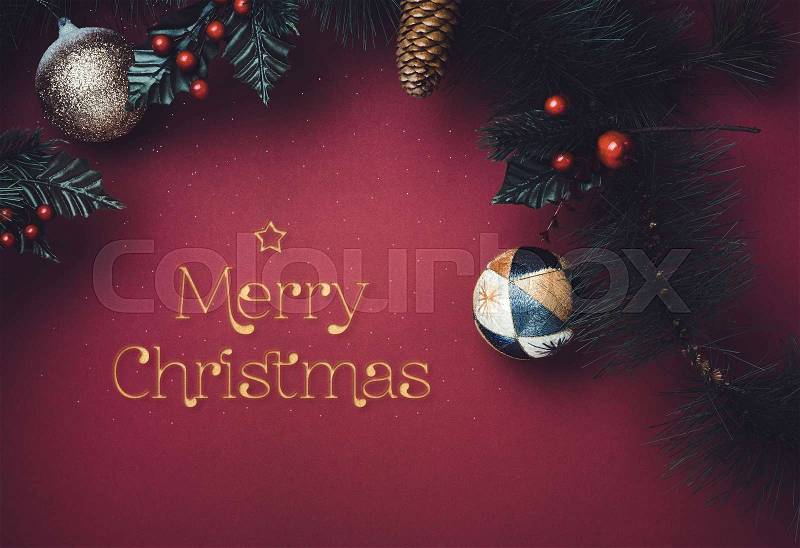 Golden sparkle Merry Christmas text with star with ball and fir branches for wreath with cherry and pine cone on dark red background. greeting card for winter holiday festive celebration concept, stock photo