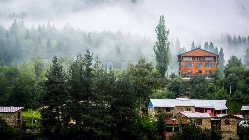 Stylish wooden house among forest in the fog, Mestia, Georgia, stock photo
