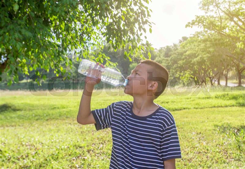 Young cute asian boy drink a water from bottle in a park during summer time with sunset, stock photo
