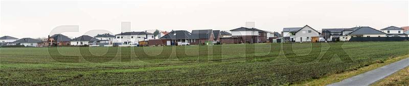 Panorama of a new housing estate with single-family houses on the edge of a village with arable land, lots of space and width as a header for a website, stitched, stock photo