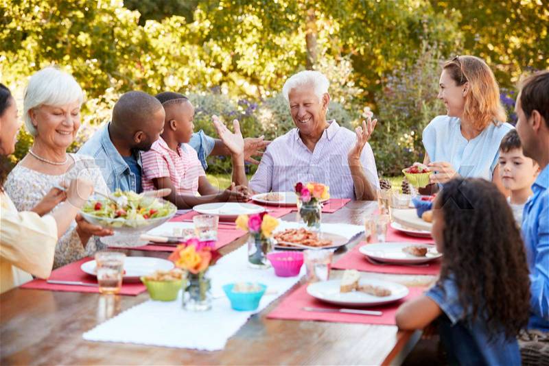 Family and friends talking over lunch at a table in garden, stock photo