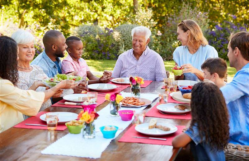 Family and friends serving lunch at a table in the garden, stock photo