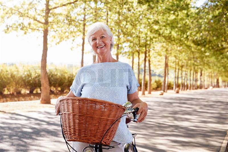 Portrait Of Smiling Senior Woman Cycling On Country Road, stock photo