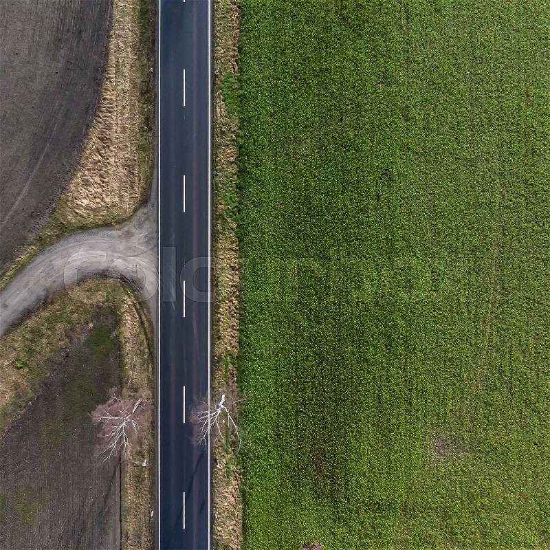 Aerial view of an asphalted country road in Germany with a farmland on the left and a green meadow on the right side. Abstract impression due to vertical angle of view. Made with drone, stock photo