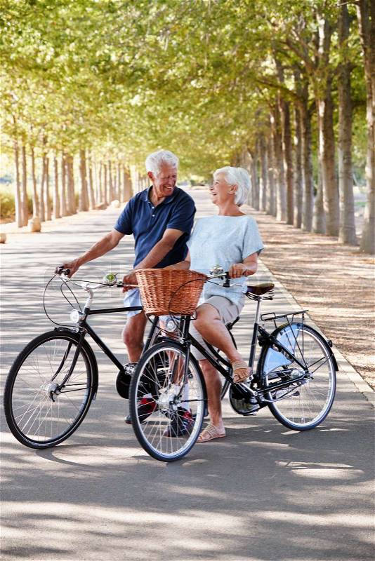 Smiling Senior Couple Cycling On Country Road, stock photo