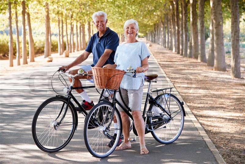 Portrait Of Smiling Senior Couple Cycling On Country Road, stock photo