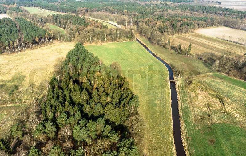 Aerial view of a stream flowing through meadows and fields with a small pine forest on one side, made with drone, stock photo