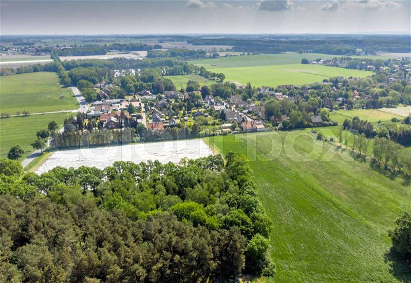 Aerial view of a small village in the distance behind a piece of forest and an asparagus field covered with foil, made with drone, stock photo