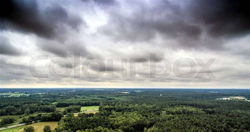Aerial view of a dense wooded area in Germany, which is crossed by a road at the edge of a city, with dramatic sky , made with drone, stock photo