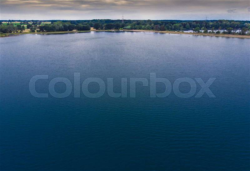Aerial view from a low altitude of a dark lake with blue water and a strip of forest and a dramatic sky on the horizon, made with drone, stock photo