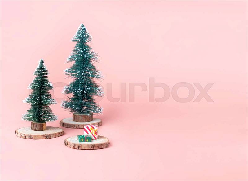 Tree Christmas tree on wood log slice with present box on pastel pink studio background.Holiday festive celebration greeting card with copy space for display of design or content, stock photo