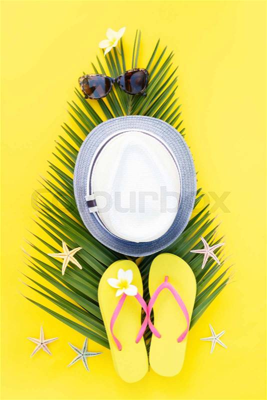Summer flat lay border with palm leaf, hat and green leaves on yellow background, stock photo