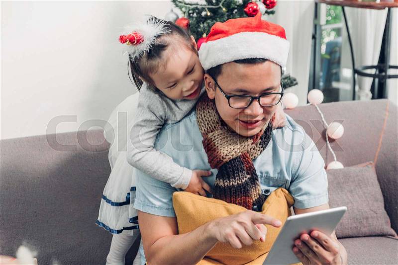 Father and daughter sitting on sofa and select christmas present and shopping from online store by tablet at xmas party,holiday gift giving festive, stock photo